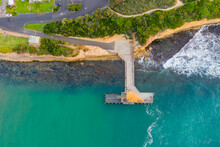 Aerial View Of A Road Running Down To A Sea Jetty Over Deep Blue Water