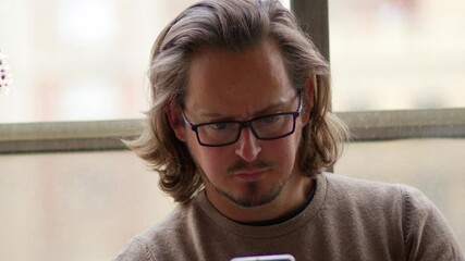 Millennial Man Long Hair attractive wearing glasses reading serious concentrated mobile phone message at home on autumn winter day portrait shot