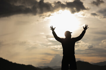 Silhouette Young man raised hand in the air with success goal on sunset background. Man standing on top of the mountain freedom life concept.