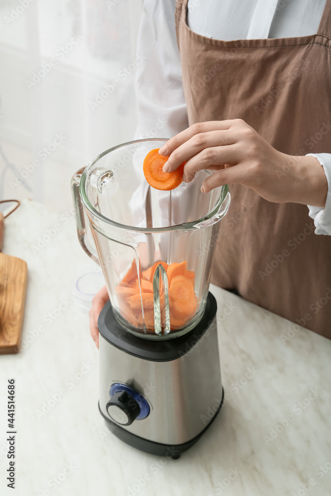 Woman preparing tasty carrot smoothie in kitchen