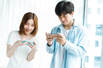 Wall Mural - Young Asian couple playing games together on mobile phones