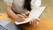 © bongkarn - Close up view of female handwriting on schedule book while working with laptop