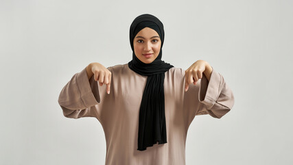 Wall Mural - Happy young arabian woman in hijab pointing fingers down