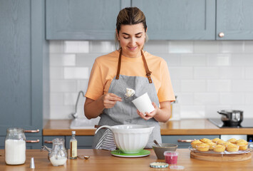 culinary, baking and people concept - happy smiling young woman cooking food on kitchen at home with cupcakes making topping of whipped cream or mascarpone cheese