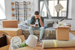 © Syda Productions - moving, eviction and real estate concept - sad man with smartphone and boxes at new home