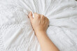 Woman hand gripping hard with visible blood vein on white bed sheet.