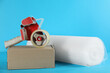 Bubble wrap roll, tape dispenser and cardboard box on light blue background
