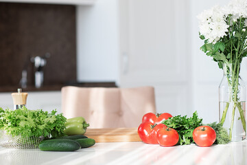 Ingredients and tools for fresh healthy vegetables salad. The concept of home cooking. Green salad, cucumbers, red tomatoes, flowers on the table on white kitchen. Sunny kitchen. Copy space,background