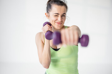 Wall Mural - Portrait of a beautiful and confident athletic woman exercising with dumbbells at white room. Training fitness or aerobics