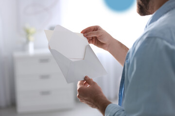 Man holding envelope with greeting card at home, closeup