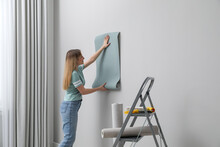 Woman Hanging Stylish Wall Paper Sheet Indoors