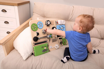 Wall Mural - Cute little boy playing with busy board on sofa at home