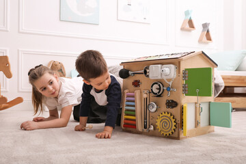 Wall Mural - Little boy and girl playing with busy board house on floor in room