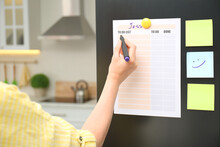 Woman writing to do list on refrigerator door in kitchen, closeup
