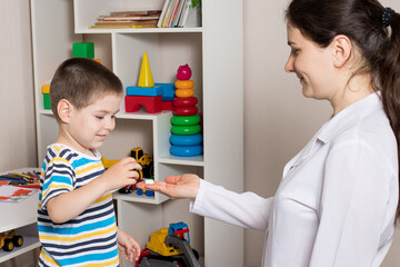 A female pediatrician or nurse gives a child a white vitamin pill. Dietary supplements for children, vitamins.