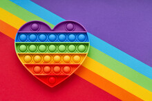 Colorful Trendy Pop It Heart Shape Fidgets Toy For Kids On A Rainbow Background. Flat Lay