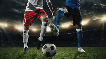 Two male soccer, football players dribbling ball at the stadium during sport match on dark sky background.