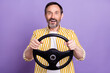 © deagreez - Photo of positive amazed happy mature man hold hands steering wheel isolated on purple color background