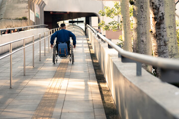 person in wheelchair in the middle of ascending ramp to train station.