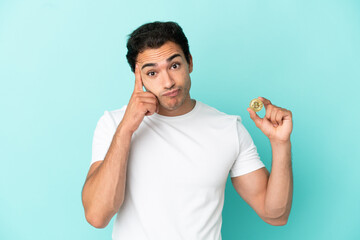 Sticker - Young man holding a Bitcoin over isolated blue background thinking an idea