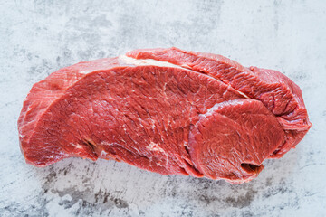 Raw beef meat in one piece against the background of a gray kitchen countertop.