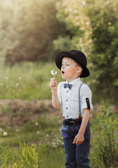 Wall Mural - A little boy in a hat blowing on a white dandelion. Child in retro clothing. Vertical