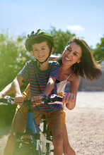 Happy Mother With Son Riding Bicycle In Sunny Driveway