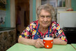 Portrait of a cheerful old woman with a cup of coffee in the kitchen at home. 