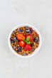 Bowl of chocolate granola with blueberries and strawberry on grey top view. Healthy breakfast. Flat lay minimalist design. Space for text.