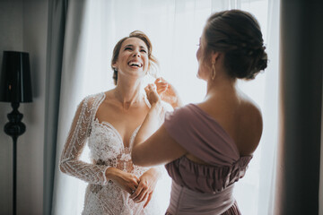 Wall Mural - Bridesmaid helping the bride to get dressed for the wedding ceremony