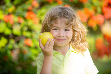 Portrait of little boy holding and eating an apple over green nature background.