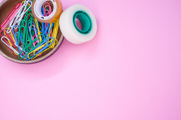 Sticker - Top view of colorful paper clips and adhesive tapes in a wooden bowl on a pink background