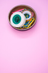 Poster - Vertical shot of colorful paper clips and adhesive tapes in a wooden bowl on a pink background