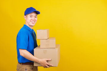 Wall Mural - Portrait excited attractive delivery happy man logistic standing smile wearing blue t-shirt and cap uniform holding parcel box looking to camera, studio shot isolated on yellow background, side view