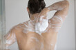 © fizkes - Back of handsome athletic wet young man taking shower, rubbing muscular body with foamy sponge, soap, cleansing gel. Male morning bath routine, daily hygiene, bodycare concept. Rear view