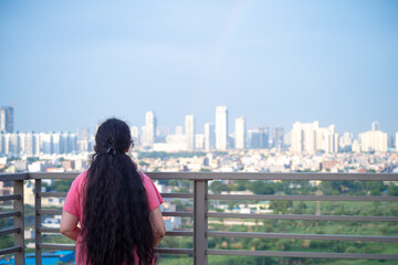 Zoomed in shot of indian woman with long hair in front of huge towers skyscrapers buildings with offices homes and shopping malls in gurgaon showing the real estate and property 