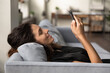© fizkes - Close up of smiling Caucasian woman relax on couch at home use cellphone shopping online on gadget. Happy millennial female rest on sofa browse wireless internet on smartphone. Technology concept.