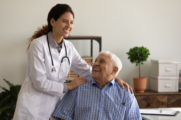 Smiling caring young female nurse comfort old Caucasian 80s male patient in private hospital. Happy woman doctor or GP support caress mature man client in clinic. Good medicine, healthcare concept.
