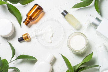 Wall Mural - Natural Cosmetic laboratory. Cosmetic bottles, cream, serum, sea salt and green leaves at white table. Flat lay image.