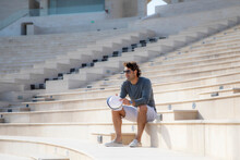 A Caucasian Solo Traveller (man) Seating On Steps And Looking Forward In The Amphitheater In  Doha Qatar On Sunny Day