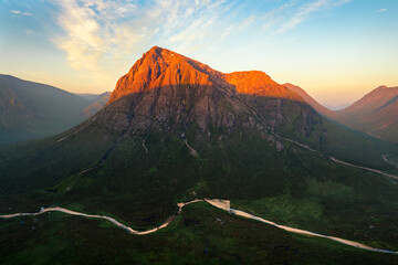 Iconic mountain peak Buachaille Etive Mor covered in beautiful golden light on a fresh Summer morning with meandering river in valley. Glencoe, Scottish Highlands, UK.