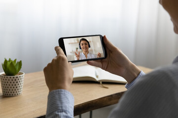 Canvas Print - Rear shoulder view young woman holding mobile phone in hands, holding distant video call conversation with indian female colleague, discussing working issues or talking with friend remotely.