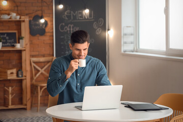 Sticker - Handsome young man drinking coffee while working with laptop in cafe