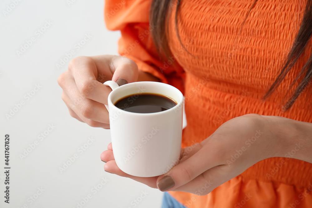 Young woman drinking coffee on light background, closeup
