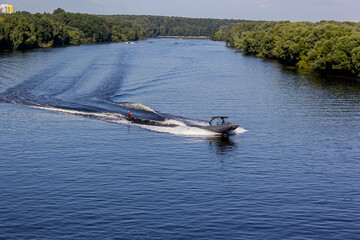 Speedboat towing an athlete on a Board against the background of the forest. Athlete water skiing and having fun. Speed boat for Surfing the Wakeboard. Water skiing on lake behind a boat. Top view