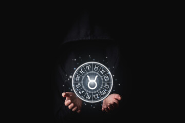 Wall Mural - a woman in a black mantle with her palms holds the glowing astrological signs of the zodiacs on a bl