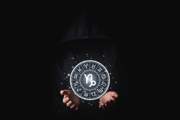 Wall Mural - a woman in a black mantle with her palms holds the glowing astrological signs of the zodiacs on a bl