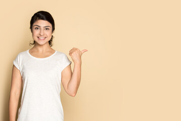 Portrait of smiling young Indian young woman isolated on yellow studio background show pint at empty vacant copy space. Happy mixed race female recommend good deal or promotion discount offer.