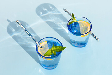 summer drink. cool refreshing beverage with mint and lemon in colored glass with paper tube. zero waste home. minimalism. natural fresh lemonade with hard shadows on blue background