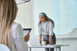 © insta_photos - Middle aged Asian businesswoman coach ceo presenting project research financial results to interns colleagues business partners team standing at table using laptop looking at screen in modern office.